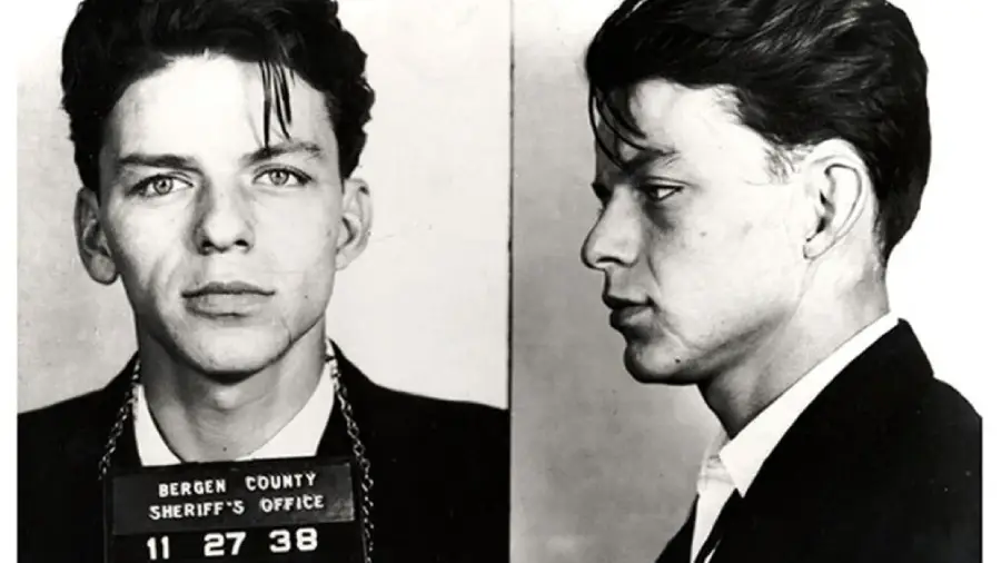 Two black-and-white mugshot photos of a young man with dark hair, wearing a suit jacket and open-collared shirt, facing front and right. The sign reads "Bergen County Sheriff's Office 11 27 38".