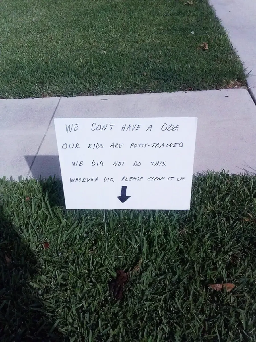 A handwritten sign on a lawn reads: “We don’t have a dog. Our kids are potty-trained. We did not do this. Whoever did, please clean it up.” An arrow points down at the grass.