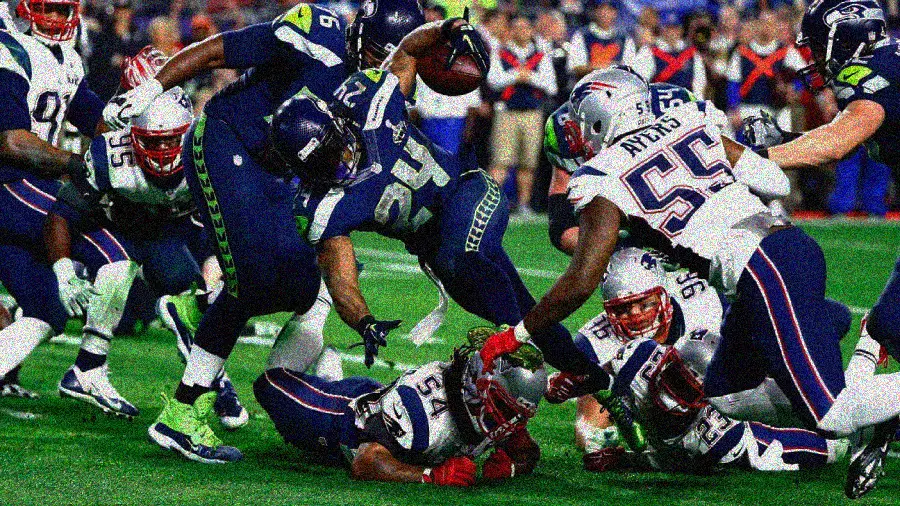 Seattle Seahawks running back rushes toward the end zone as New England Patriots defenders try to tackle him during a football game, with players colliding and reaching for the ball.