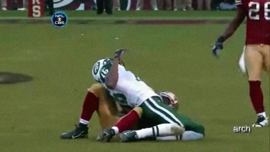 A football player in a green and white uniform collides headfirst into the back of a red-uniformed player during an NFL game, resulting in an awkward and forceful tackle on the field.