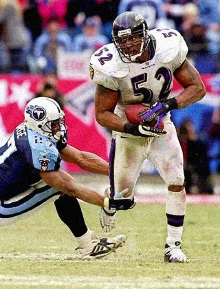 A football player in a white jersey with number 52 runs with the ball as a defender in a light blue jersey tries to tackle him during a game on a grassy field.