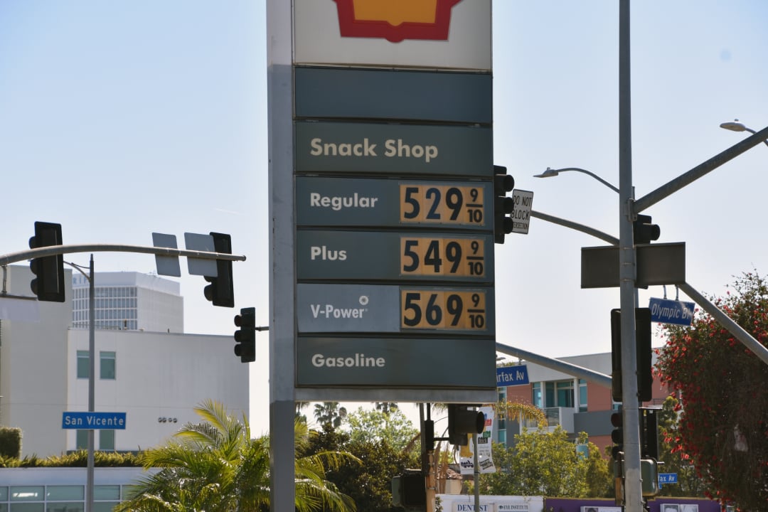 A gas station price sign displays Regular at $5.29, Plus at $5.49, and V-Power at $5.69 per gallon. Traffic lights and street signs for San Vicente and Olympic Blvd are visible in the background.