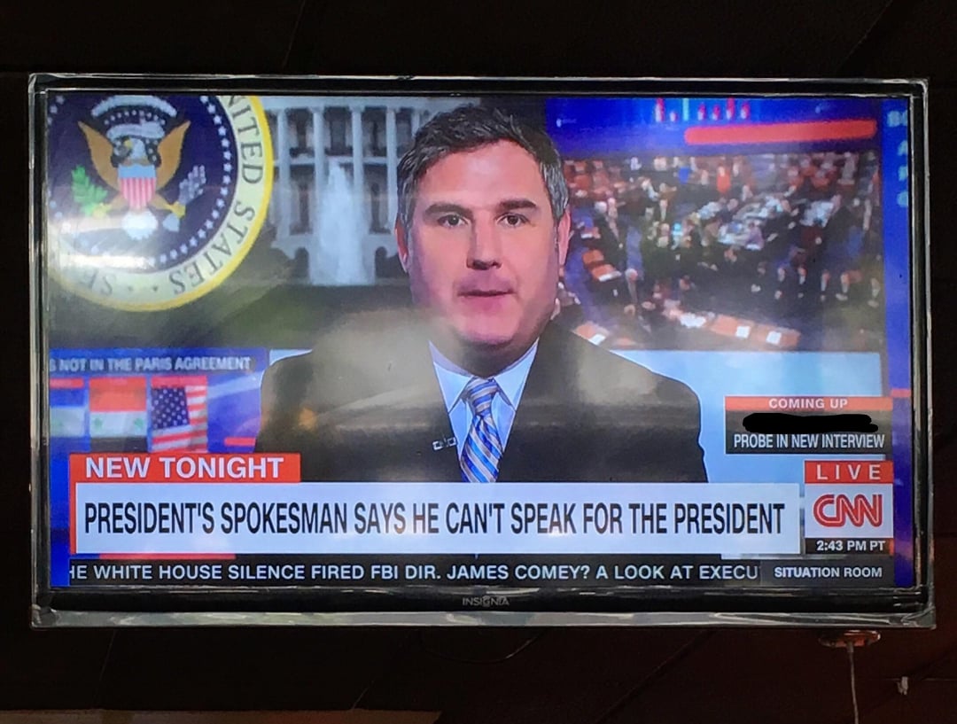 A TV displays a CNN news broadcast featuring a male anchor. The headline reads, "President's spokesman says he can't speak for the president." The background includes the presidential seal and newsroom images.