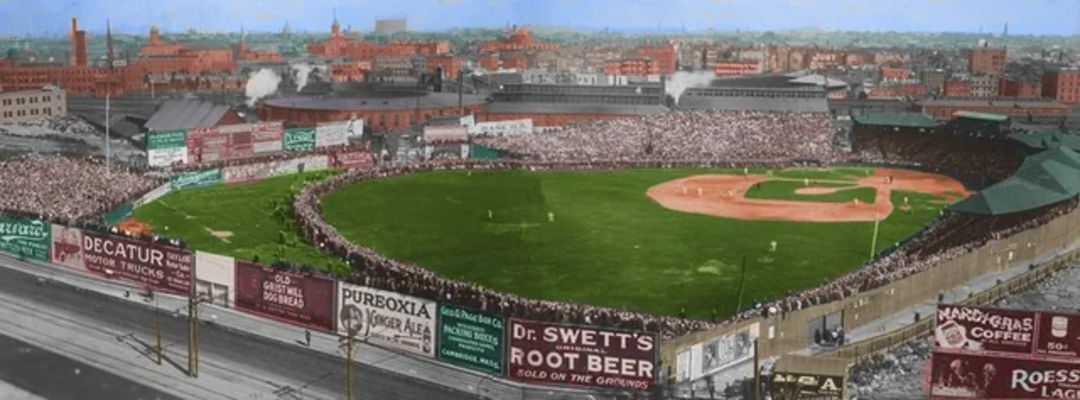 A crowded early 20th-century baseball stadium, surrounded by colorful vintage advertisements, with a game in progress and a cityscape visible in the background.