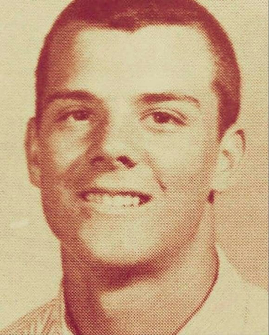 A sepia-toned portrait of a young person with short hair, smiling slightly at the camera. The individual is wearing a light-colored collared shirt and appears to be photographed for a yearbook or school photo.