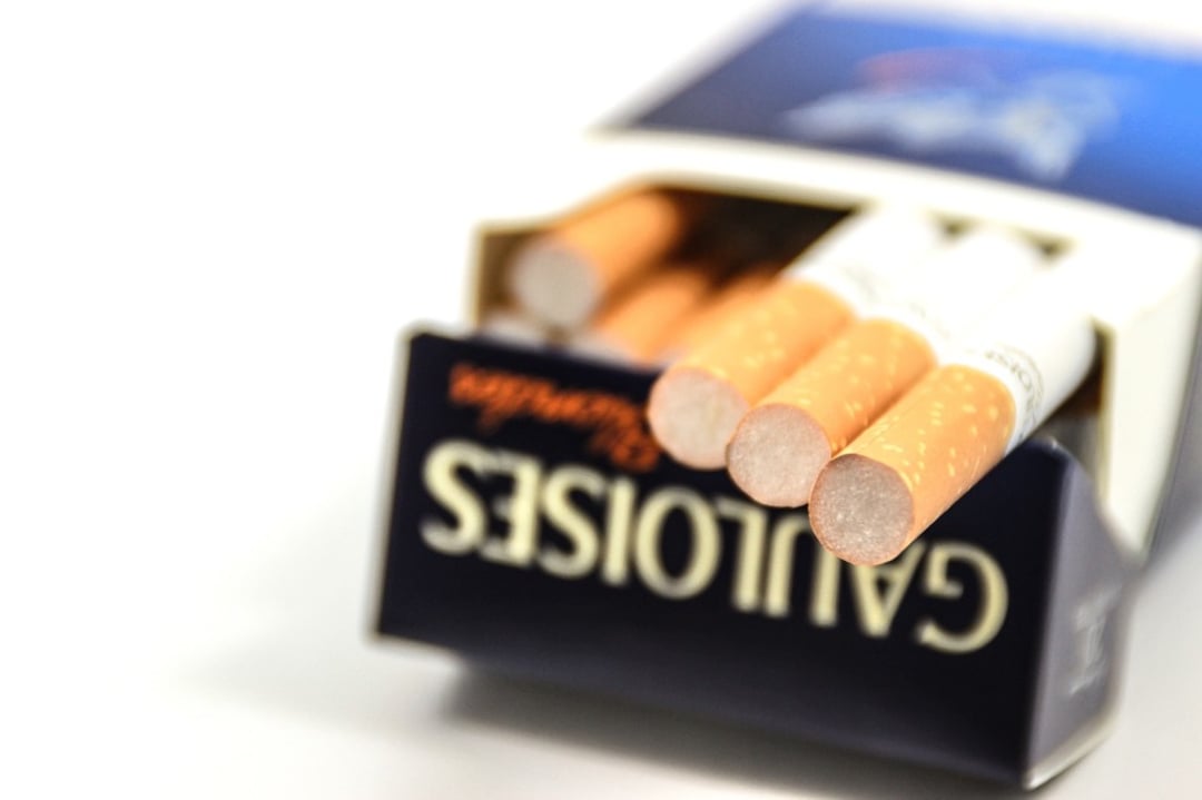A close-up of an open pack of Gauloises cigarettes with several filter-tipped cigarettes visible, some protruding from the pack. The pack is mostly blue with white and orange accents.