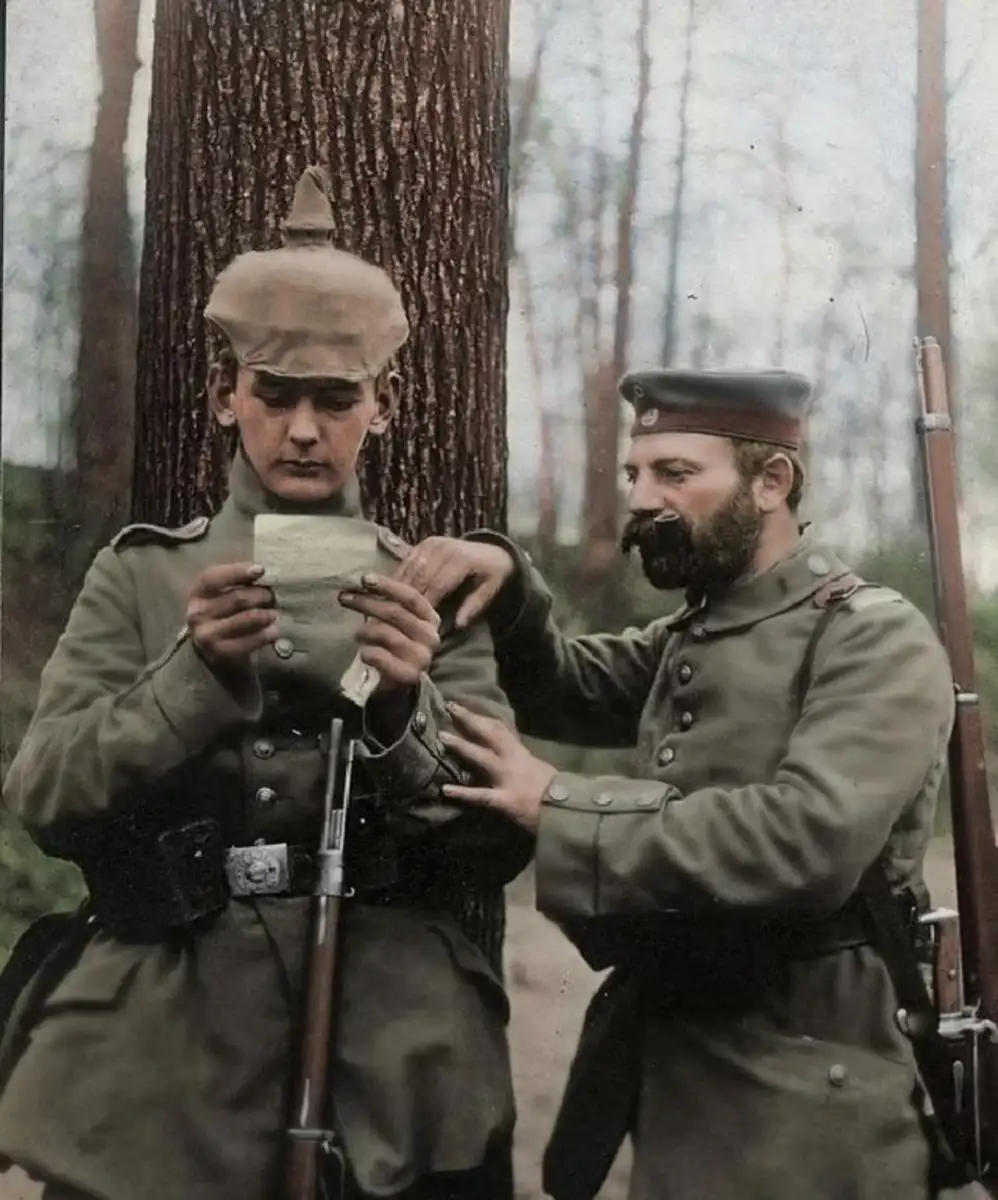 Two World War I soldiers in uniforms stand in a forest; one reads a letter while the other, with a beard, looks on and lightly touches his arm. Both have rifles and somber expressions.