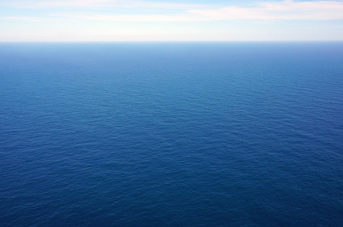 Calm, endless blue ocean stretching to the horizon under a light blue sky with a few wispy clouds.