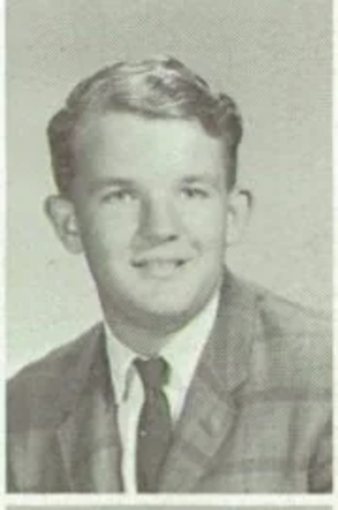 A young man with short, neatly combed hair is wearing a plaid jacket, dress shirt, and tie. He is smiling slightly and posing for a formal portrait against a plain background. The image appears to be from a yearbook.