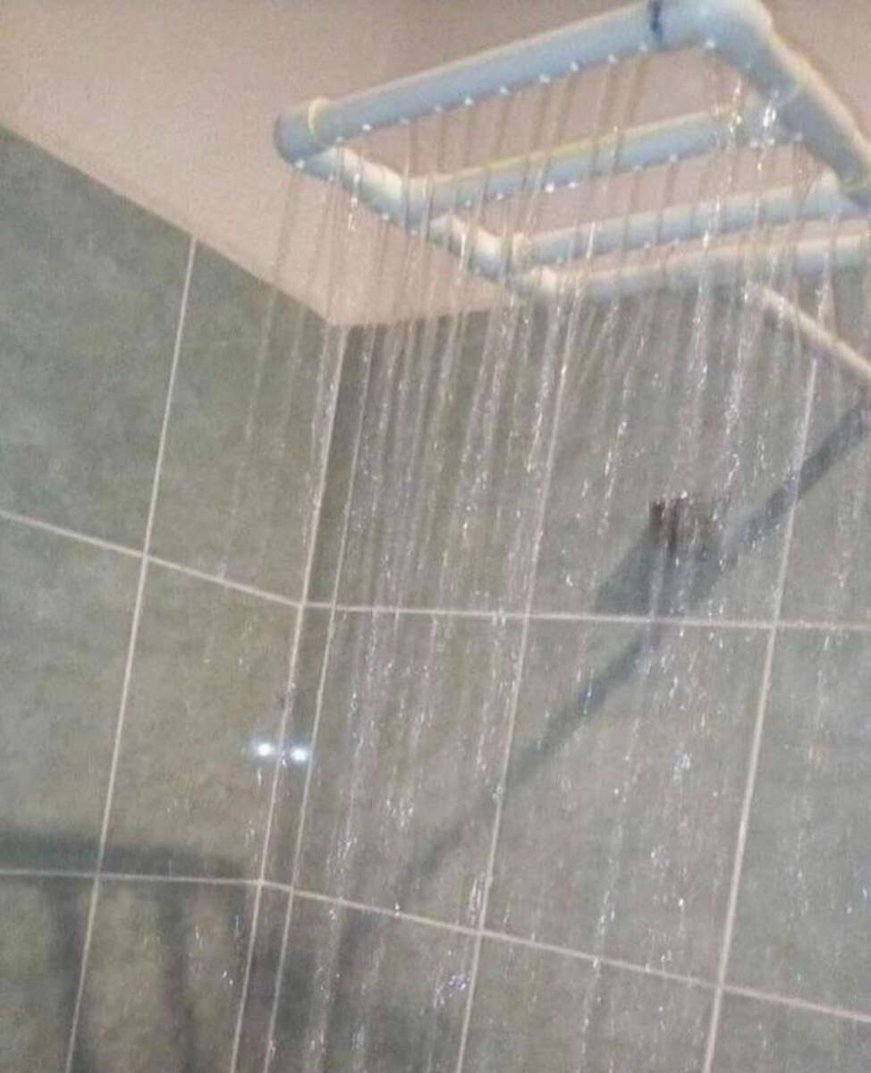 A homemade showerhead made from white PVC pipes with holes, creating multiple streams of water, is mounted on a tiled bathroom wall.
