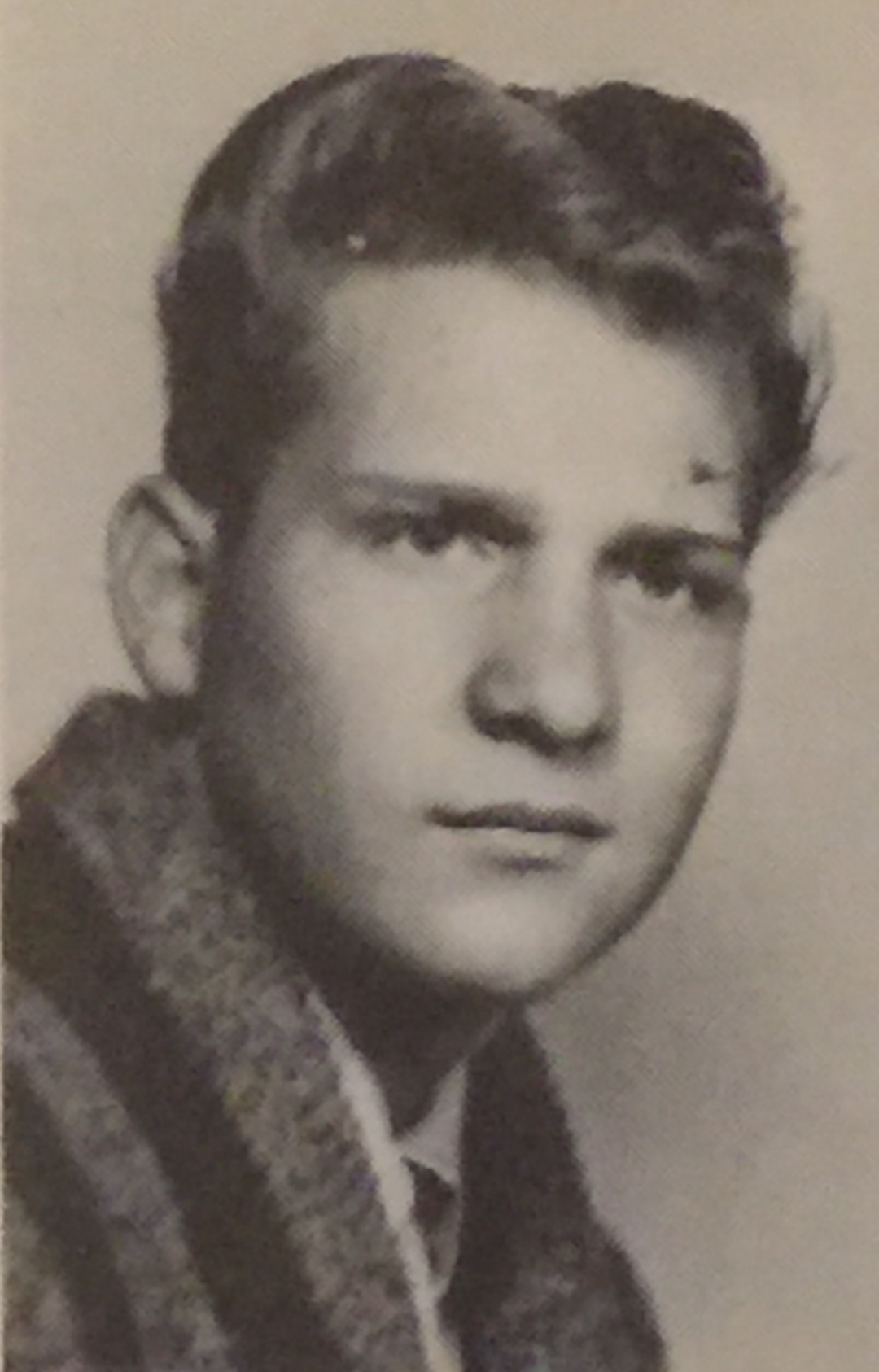 Black and white portrait photo of a young person with short, wavy hair, wearing a collared shirt and textured jacket, looking slightly to the side with a neutral expression.