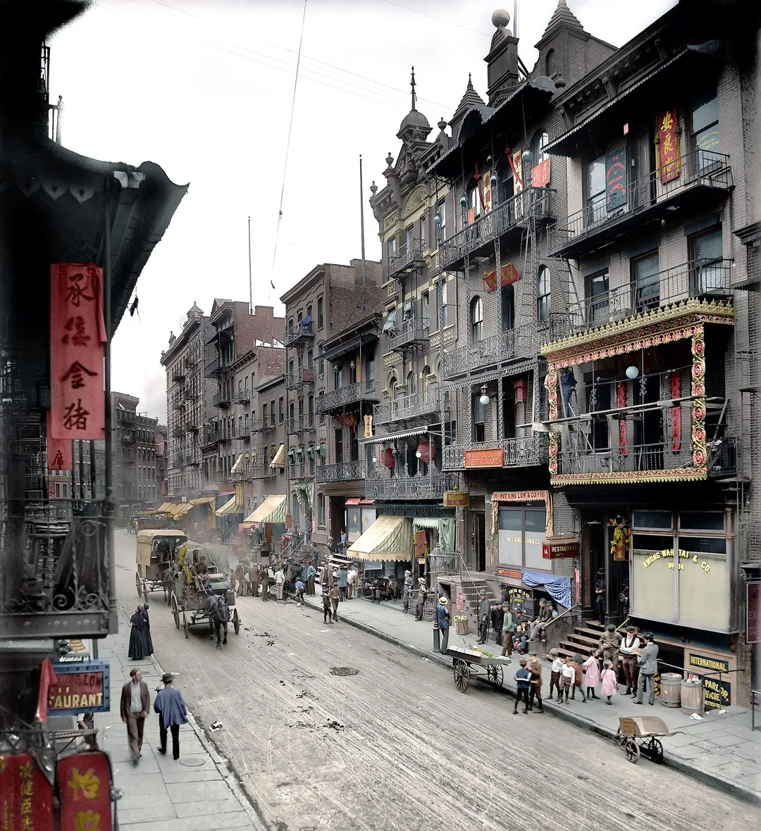 A busy street scene in historic Chinatown, New York City, with people walking, horse-drawn carriages, and ornate buildings decorated with Chinese signs, lanterns, and balconies.