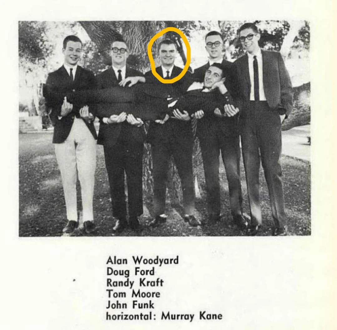 Six young men in suits stand outdoors; five are holding another man horizontally. The man being held is smiling and encircled in yellow. A caption below the photo lists their names.