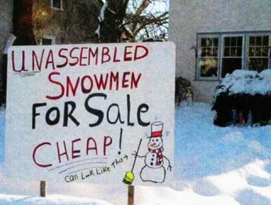 A snowy yard with a hand-painted sign reading "Unassembled Snowmen for Sale Cheap! Can look like this" with a drawing of a snowman. The sign is surrounded by snow near a house.