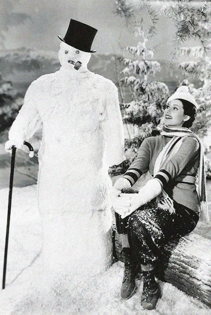 A woman in winter clothes sits on a snowy log, smiling at a snowman with a top hat, cane, and cigar. Pine trees and snow cover the background, creating a festive winter scene.
