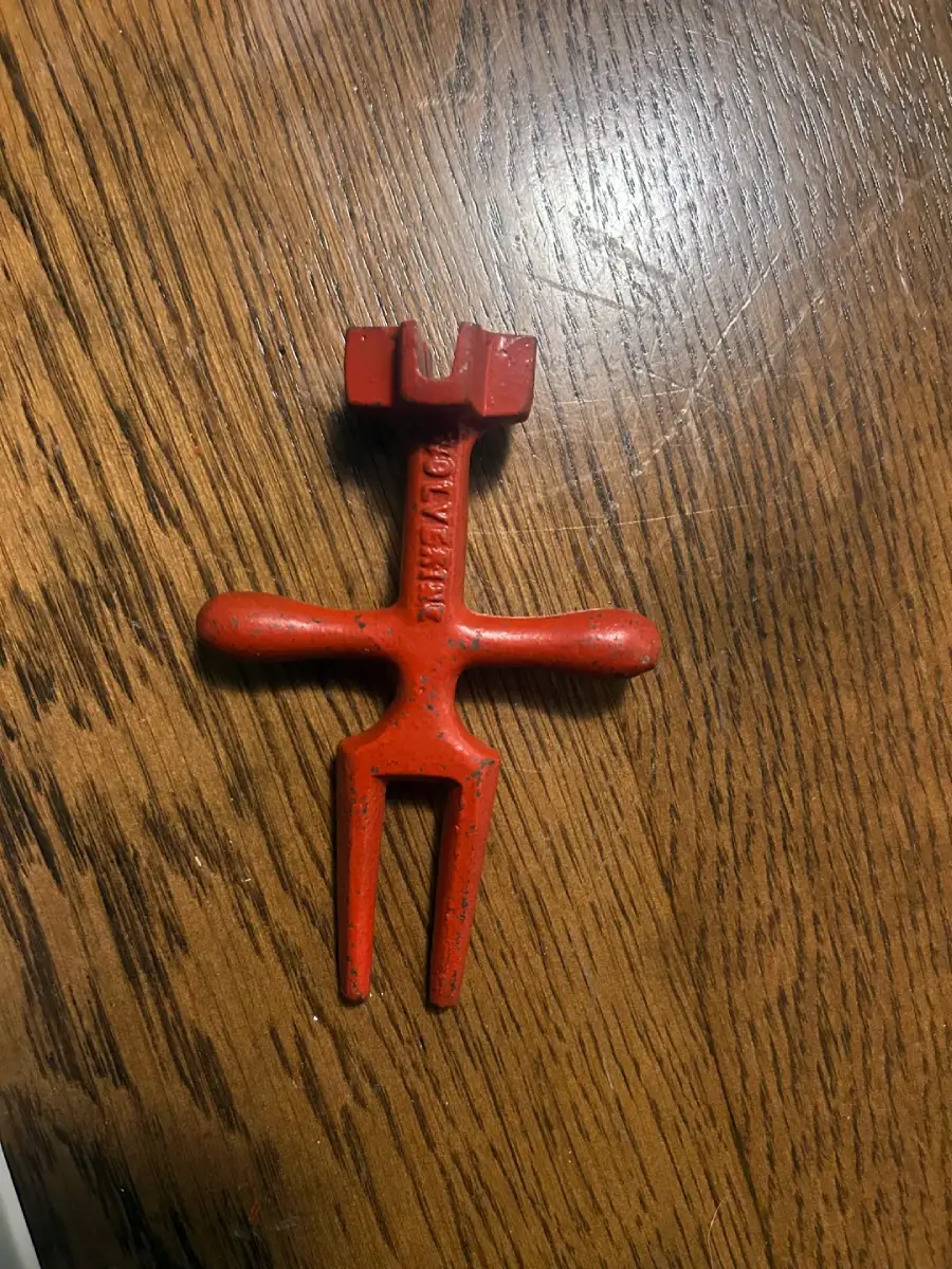 A red metal tool with two prongs at the bottom, two horizontal handles, and a notched top, lying on a wooden surface. The word "CHICAGO" is embossed on the vertical part of the tool.