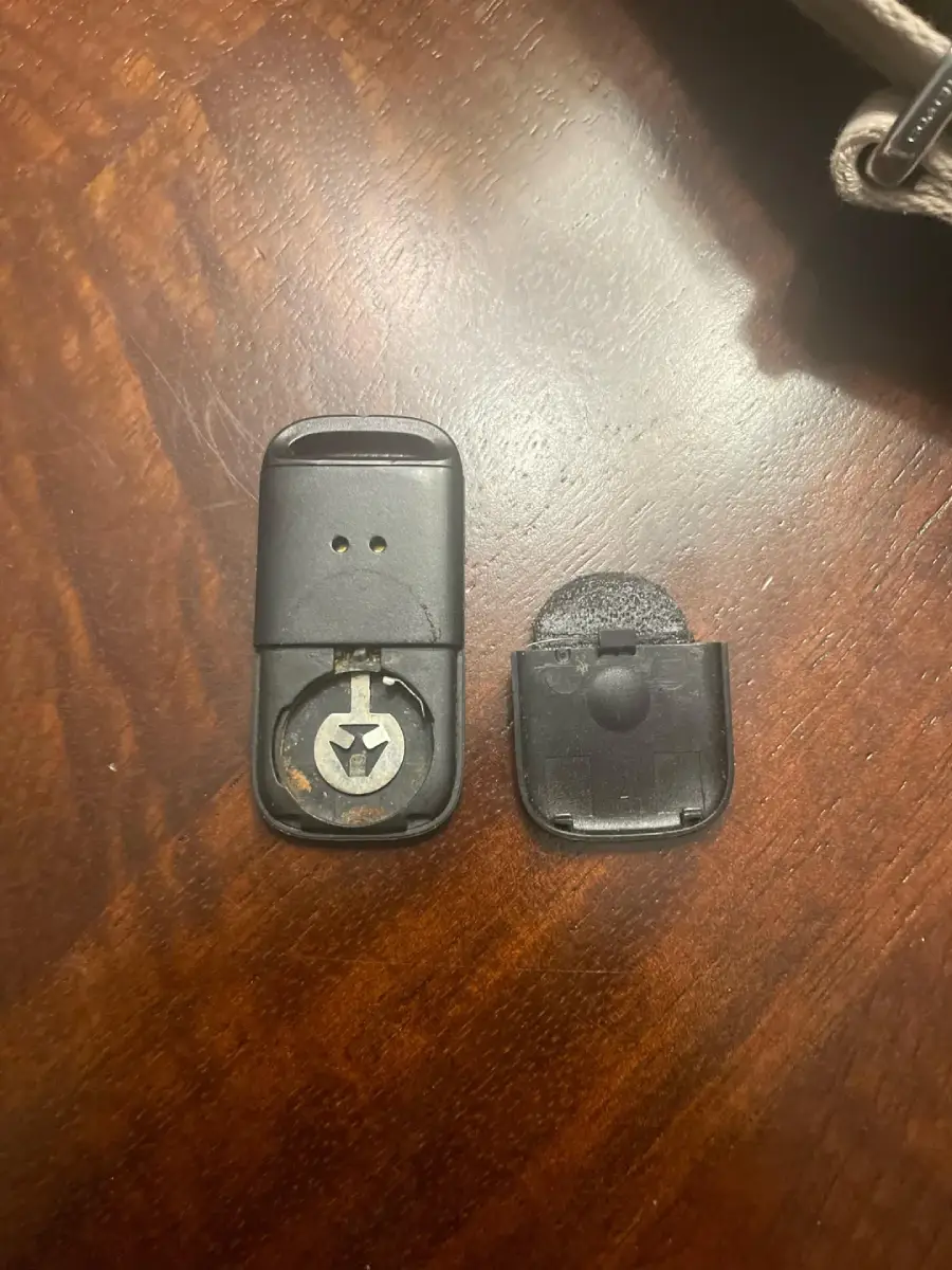 A small black plastic device, opened to show a round battery inside the left half, with the right half of the casing placed next to it on a wooden surface.