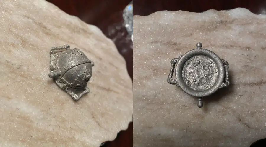 A small, metallic object shaped like a globe on a stand is shown on the left; on the right, the underside features a circular, cratered pattern resembling the surface of the Moon. Both rest on a pale, textured stone surface.