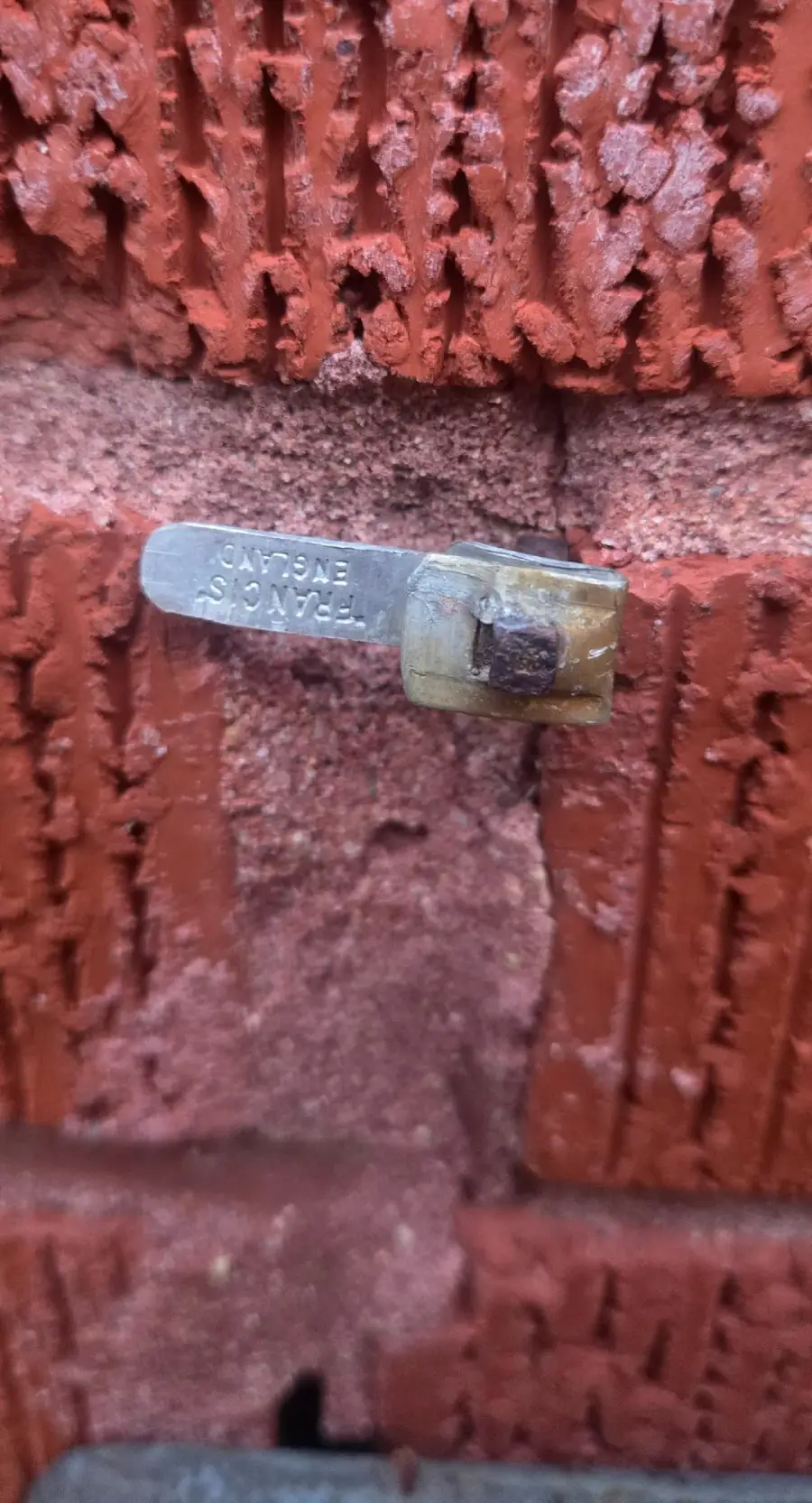 A close-up of a metal tag embedded in a red brick wall. The tag reads “TEXAS GAS” and is partly covered by a translucent, weathered plastic cap. The surrounding bricks show rough texture and mortar lines.