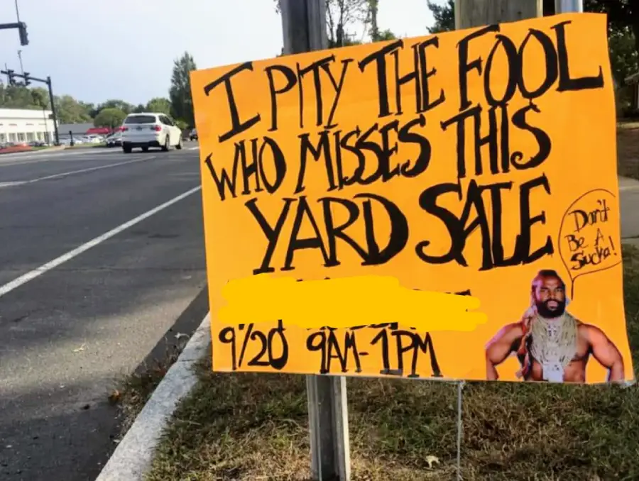 A bright yellow yard sale sign by a roadside reads, "I pity the fool who misses this yard sale. 9/20 9AM-1PM." A picture of Mr. T with his catchphrase "Don't Be A Sucka!" is in the bottom right corner.