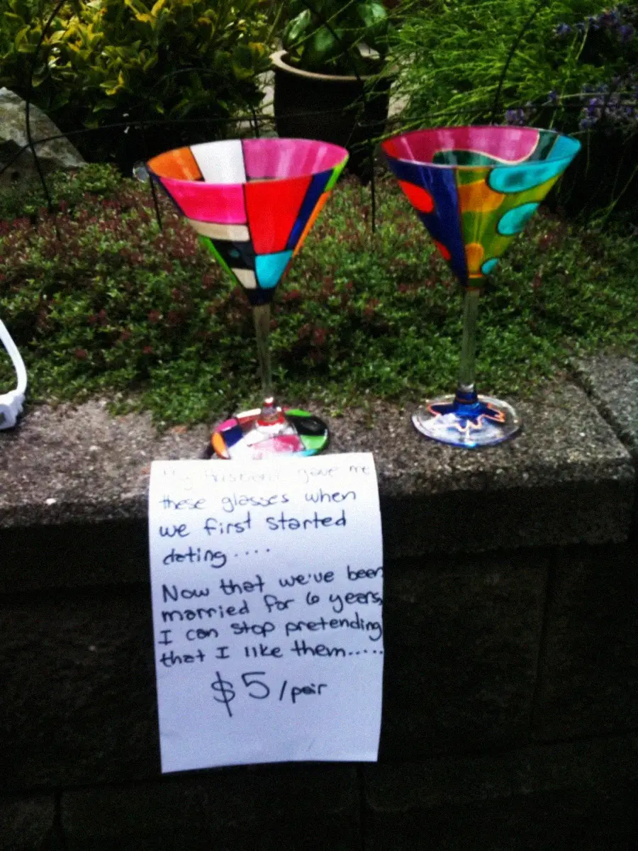 Two colorful martini glasses sit on a stone wall above a handwritten sign that reads: “You insisted I use these glasses when we first started dating… Now that we’ve been married for 6 years I can stop pretending I like them… $5/pair.”