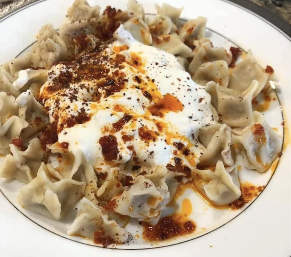 A plate of Turkish manti dumplings topped with creamy yogurt and drizzled with spiced red pepper oil and seasonings.