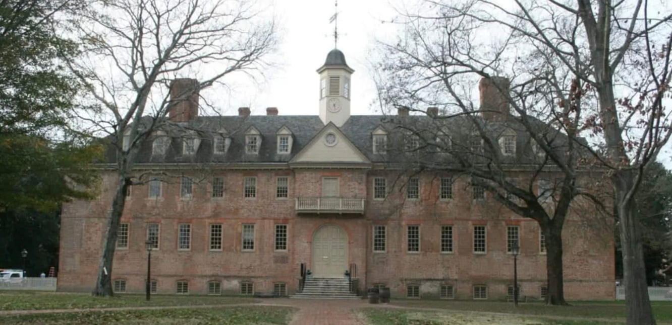 A large brick colonial-style building with symmetrical windows, a central doorway, and a cupola on the roof, framed by bare trees on either side.