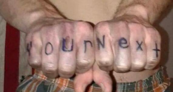 A person with bare arms and plaid shorts has the words "Your Next" written in black marker across the knuckles of both fists, which are held together and facing the camera.
