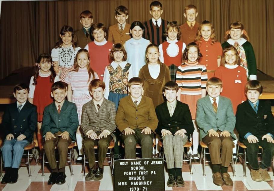 A vintage class photo of 24 smiling children and one adult teacher posed in rows on a stage. A sign in front reads: “Holy Name of Jesus School, Forty Fort PA, Grade 3, Mrs. Haughney, 1970-71.”