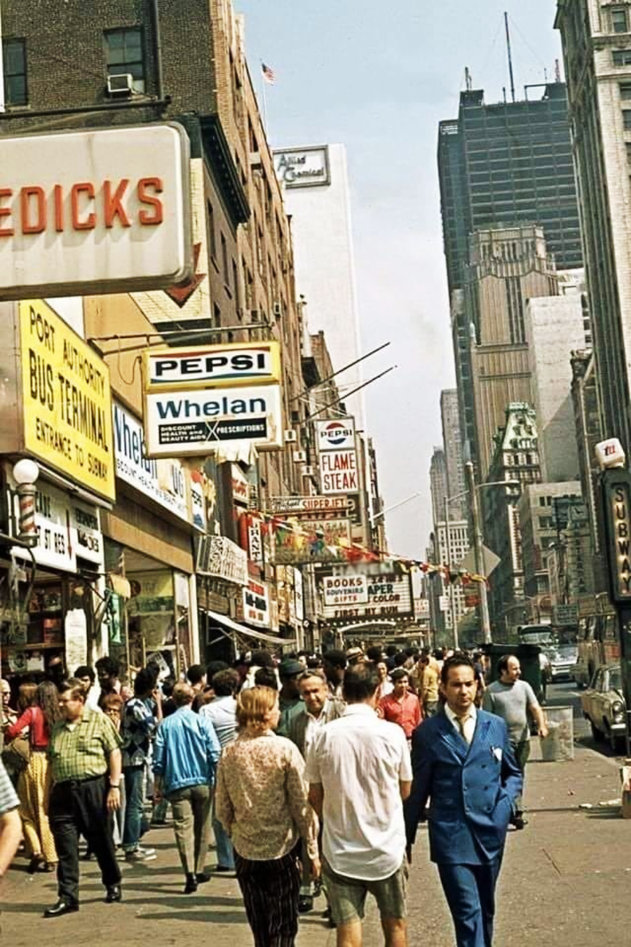 A busy city street in the 1970s, with crowds of people walking past shops, restaurants, and vintage signs, including Pepsi and Port Authority Bus Terminal, and tall buildings in the background.