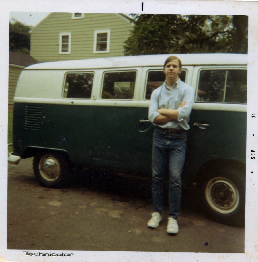A young person in jeans and a light shirt stands with arms crossed in front of a green and white vintage Volkswagen van, parked beside a beige house. The photo has a retro look and is dated September 1971.