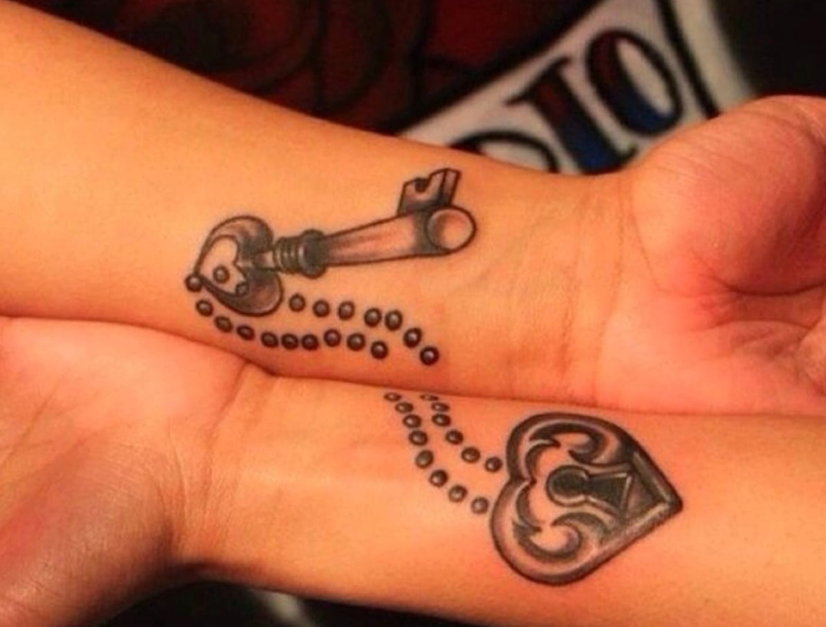 Two wrists with matching tattoos: one has a vintage key, the other a heart-shaped lock. Dotted lines connect the key and lock, suggesting they belong together.
