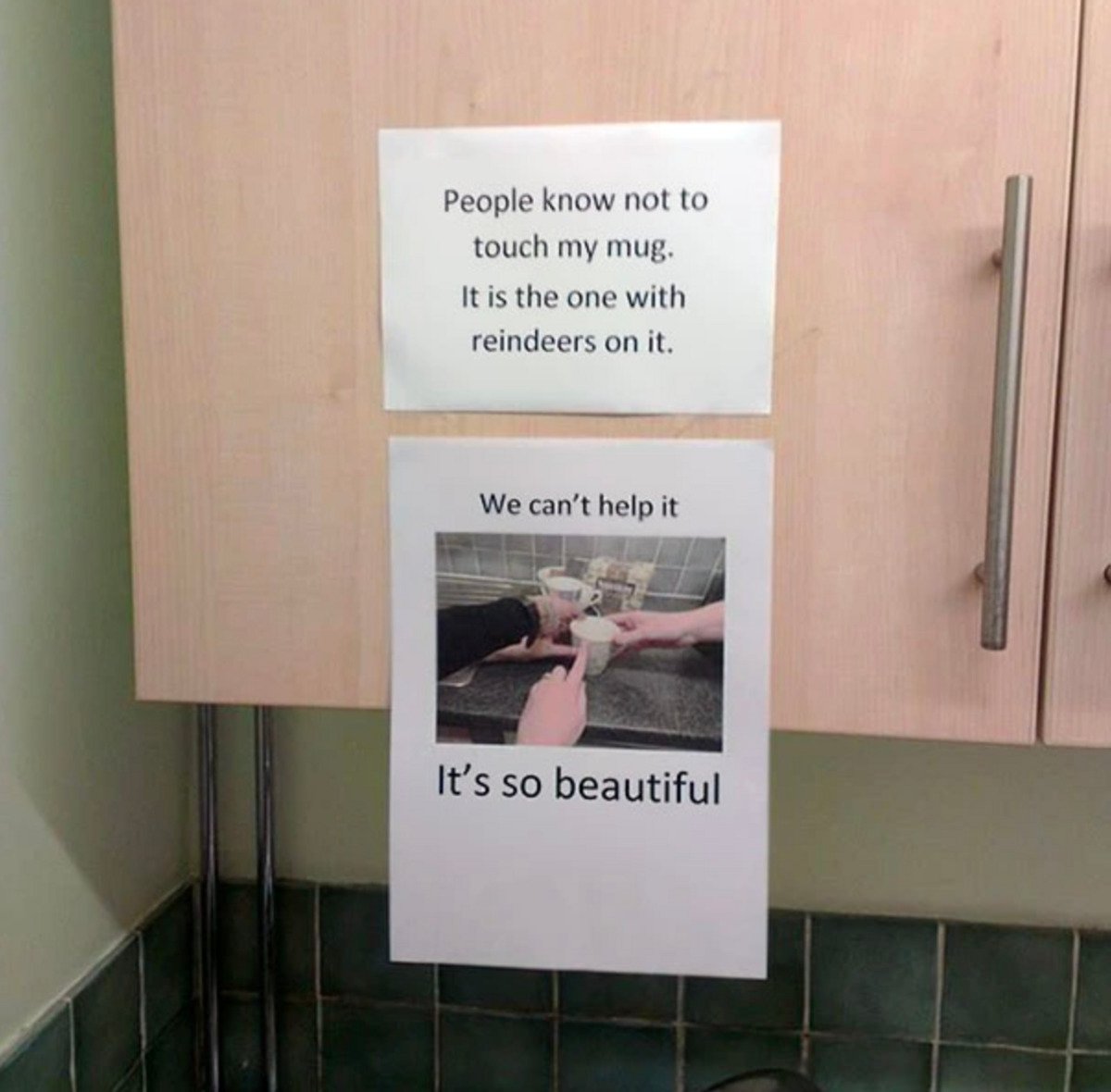 Two papers are taped to a kitchen cabinet. The top note says “People know not to touch my mug. It is the one with reindeers on it.” Below is an image of hands admiring a mug, captioned “We can't help it. It’s so beautiful.”