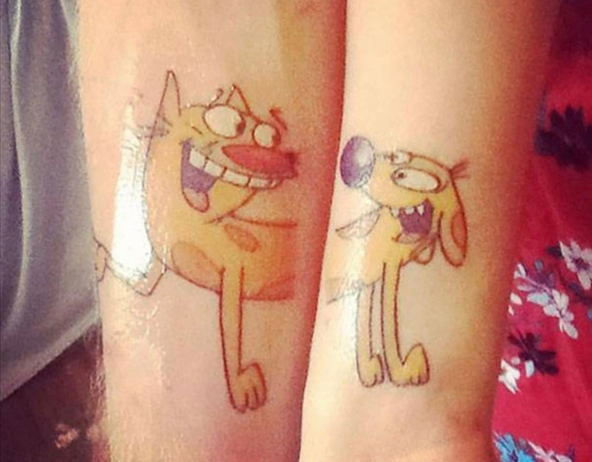 Two forearms with matching tattoos of the cartoon characters CatDog, where each arm shows one half of the character, forming the complete image when placed together.
