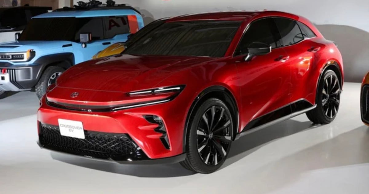 A shiny red electric crossover SUV with black accents is displayed indoors, alongside a blue vehicle in the background. The car features sleek lines, narrow headlights, and large black wheels.