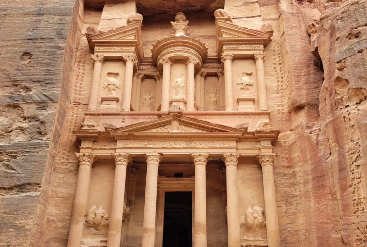 The ancient rock-cut facade of Al-Khazneh, or the Treasury, in Petra, Jordan, featuring ornate columns, statues, and intricate carvings carved into a sandstone cliff.