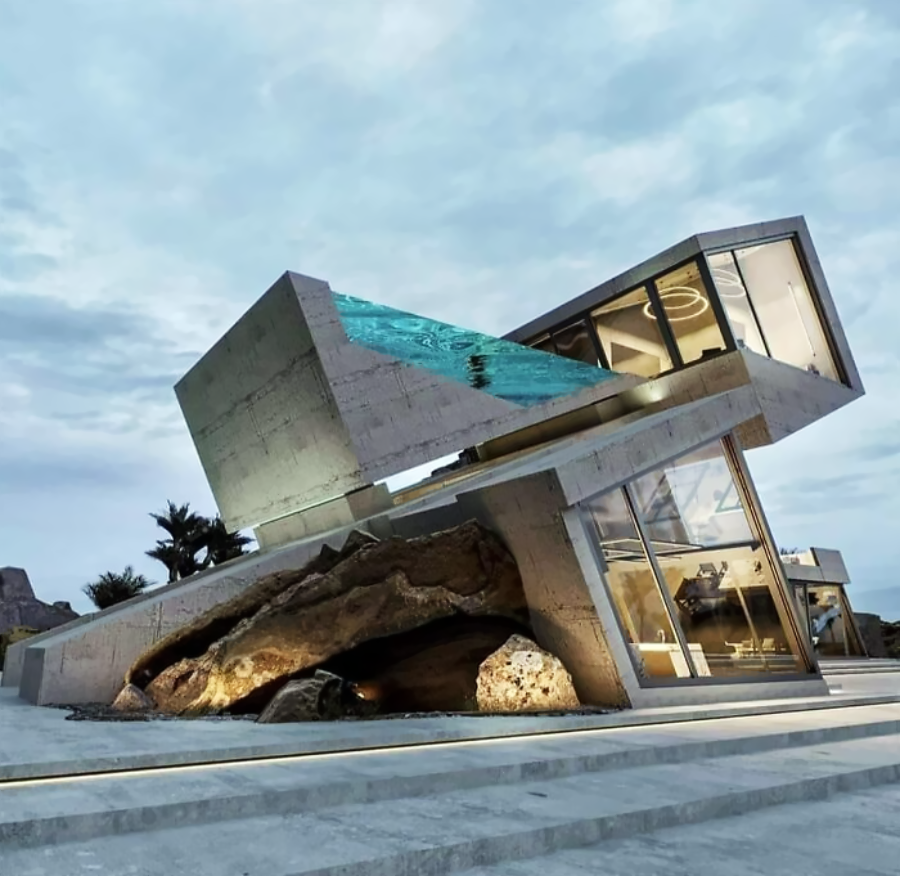 A modern, angular concrete house with large glass windows is built over a massive rock, featuring a rooftop swimming pool that extends outward, under a cloudy sky.