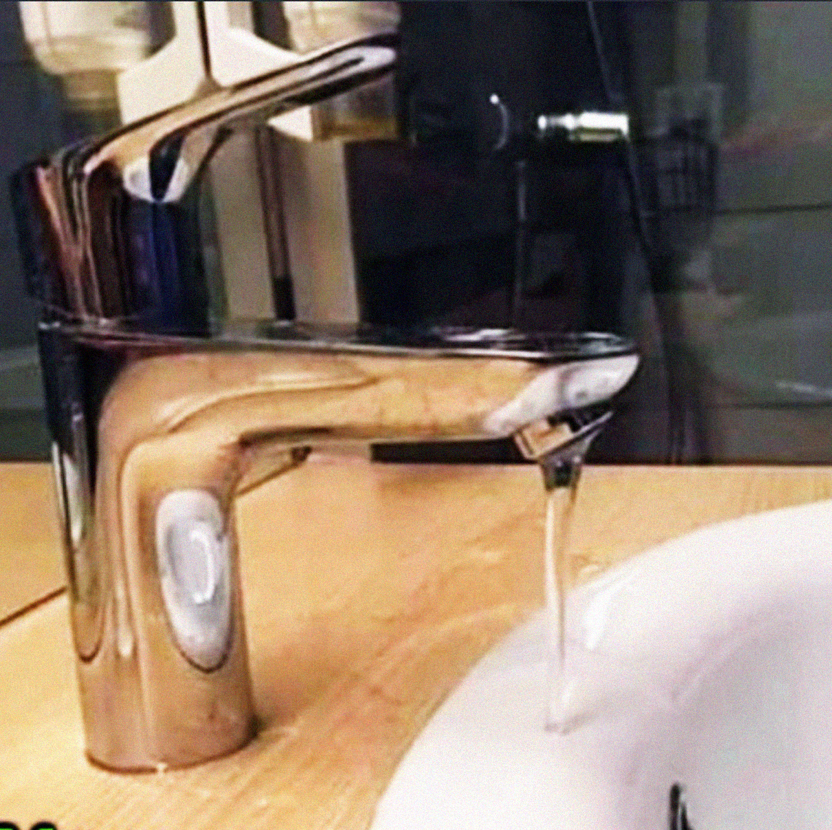 A modern chrome faucet on a bathroom sink directs water onto the counter instead of into the basin due to a misaligned spout. The countertop appears wet from the misplaced water stream.