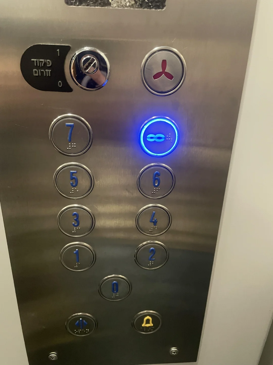 Elevator control panel with metallic buttons numbered 0 to 7, one is lit blue and marked with an infinity symbol. Two additional buttons above and a yellow bell symbol button below. Panel includes Braille next to each button.
