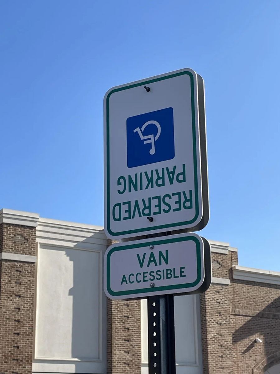 A parking sign for reserved van-accessible accessible parking is installed upside down in front of a brick building, with a clear blue sky in the background.