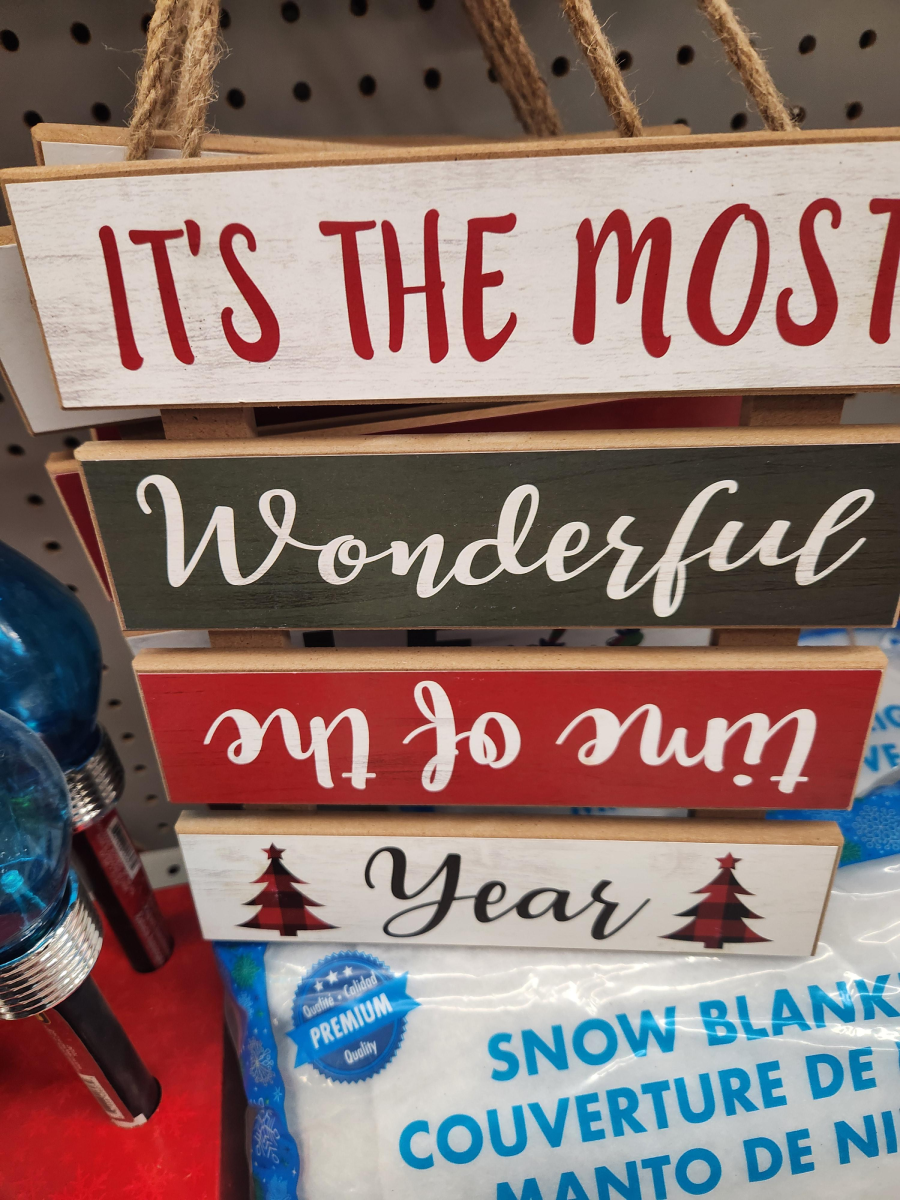 A decorative hanging sign with three wooden planks reads, "It’s the most Wonderful time of the Year," with festive colors and tree designs. The sign is positioned upside down above a package of snow blankets.