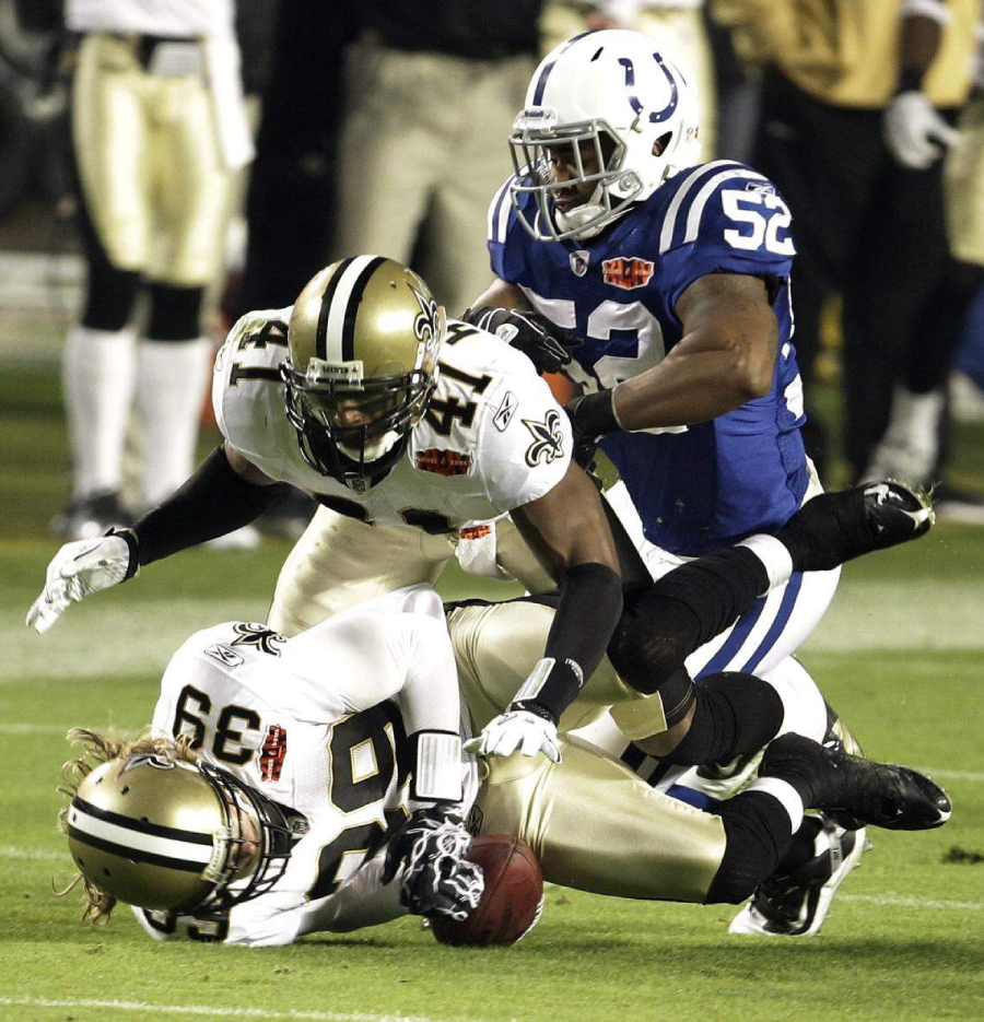 A New Orleans Saints player dives to the ground to catch a football as a teammate and an Indianapolis Colts defender in a blue uniform close in during a game.