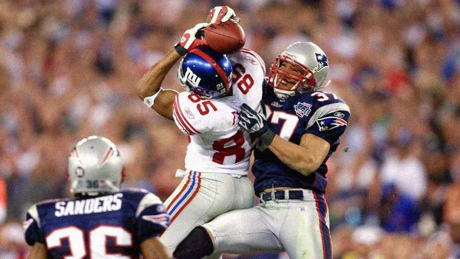 A New York Giants player catches a football while being closely defended by a New England Patriots player during an intense moment in an NFL game. Another Patriots player, number 36, is seen in the foreground.