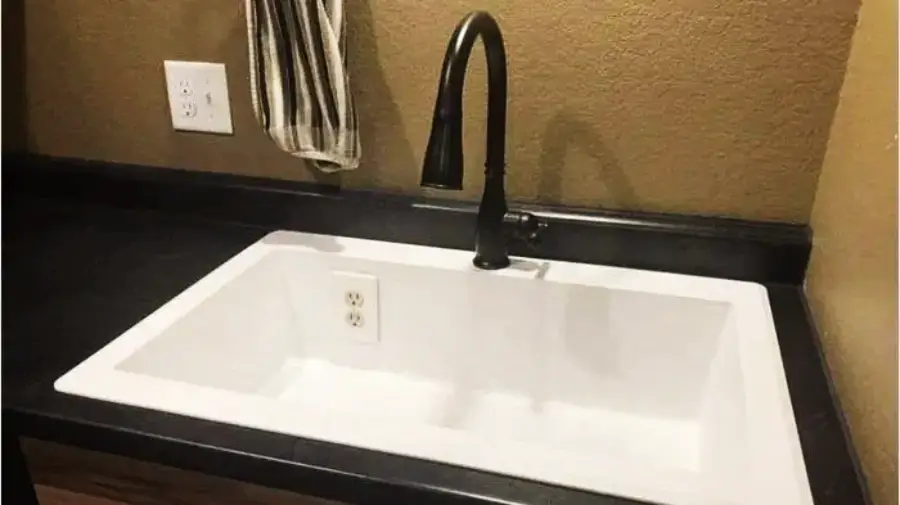 A white sink with a black faucet is installed in a black countertop. Unusually, an electrical outlet is located inside the sink basin. A striped towel hangs on the wall above another outlet.