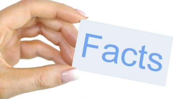 A hand with manicured nails holds a white card with the word "Facts" printed in large, light blue letters on it. The background is plain white.