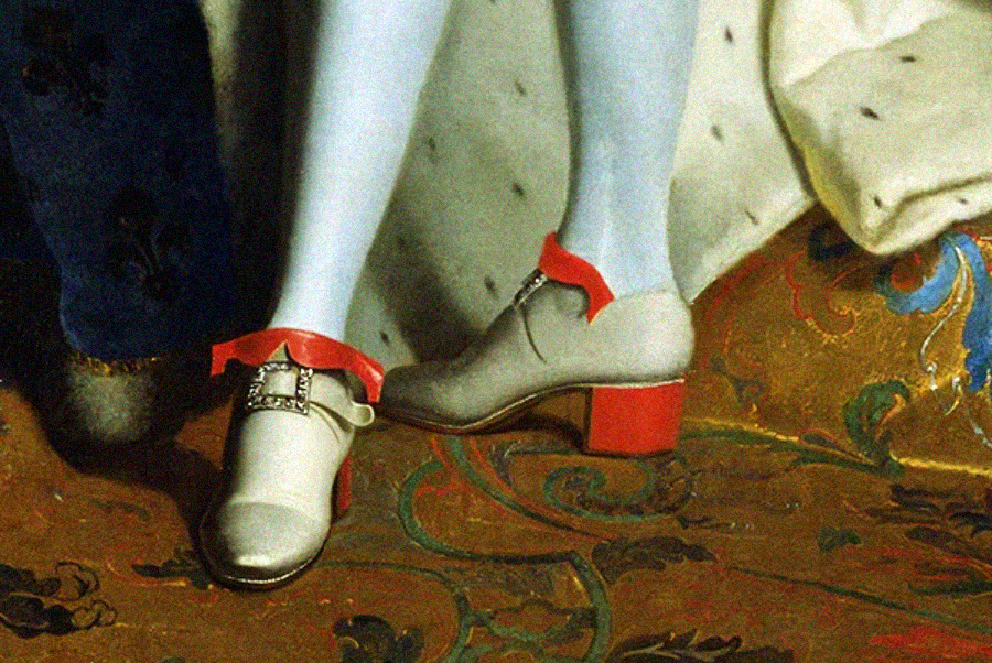 Close-up of a person's legs wearing pale stockings and light-colored heeled shoes with red heels and bows, standing on a patterned, ornate carpet. The style suggests historical European fashion.