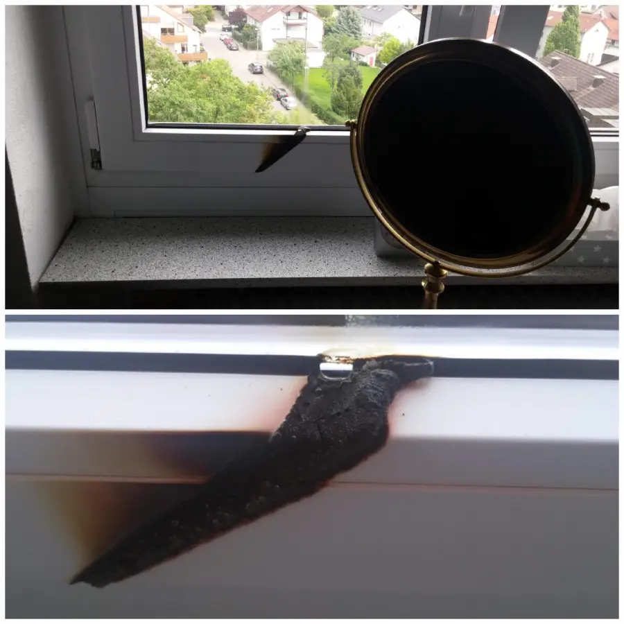 A round mirror on a windowsill reflects sunlight, causing a scorched, burned mark on the white window frame below. The burn is blackened and charred, clearly shaped by focused light.