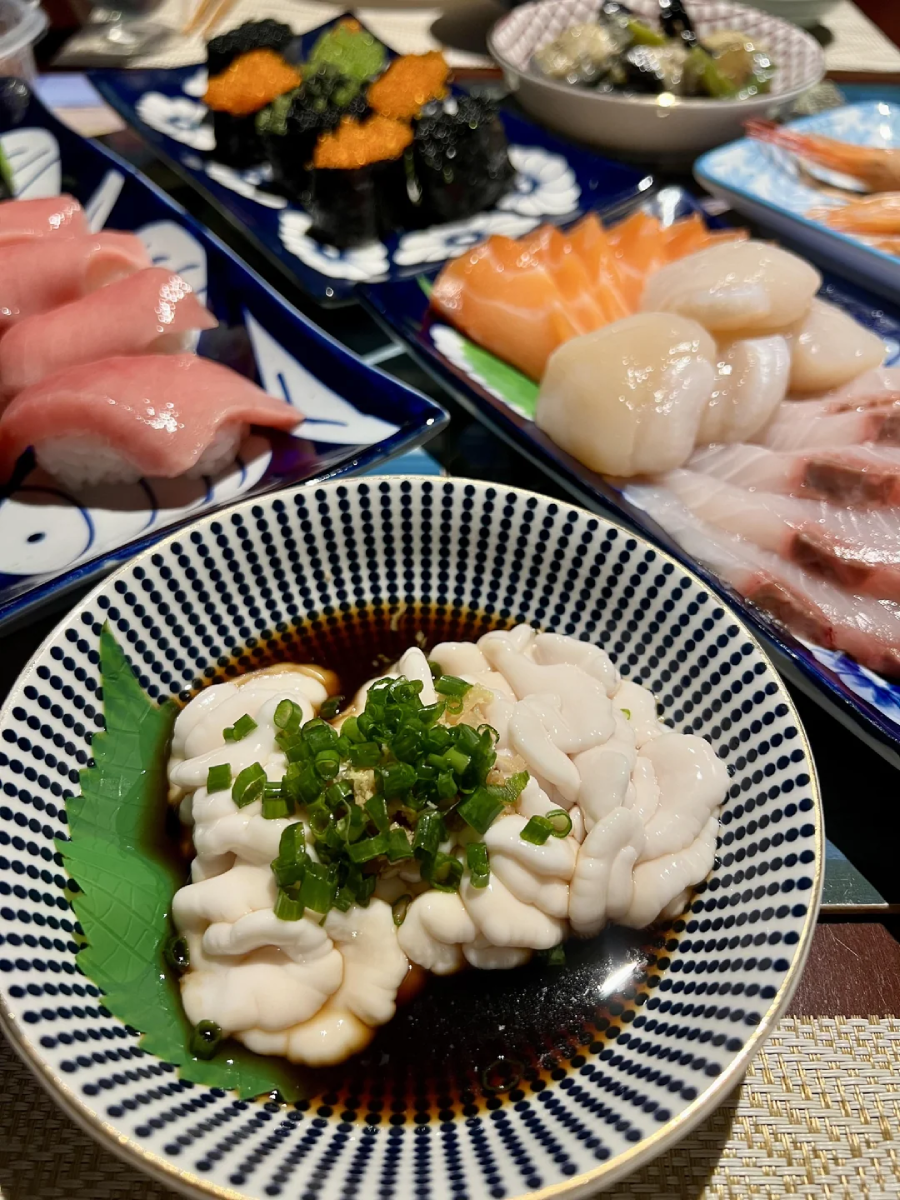 A close-up of various Japanese seafood dishes, including sushi, sashimi, and a bowl of shirako garnished with chopped green onions, served on patterned plates.