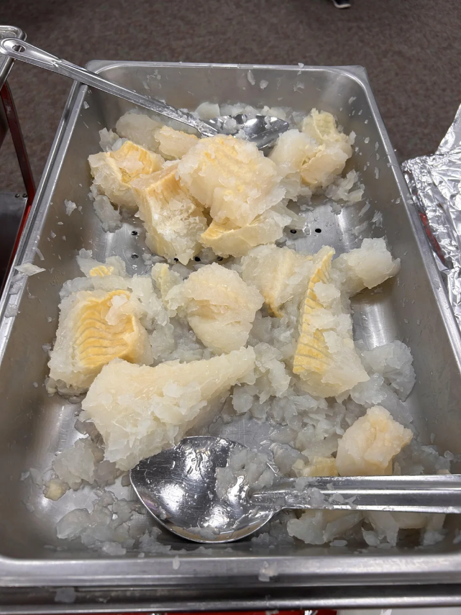 A stainless steel serving tray contains several chunks of pale, flaky fish on a bed of crushed ice, with two metal serving utensils resting inside.