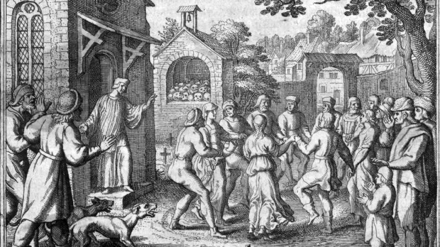A group of people, some clothed and some partially undressed, dance in a circle outside a building while others watch. A dog stands nearby and a man gestures from a doorway. Buildings and trees are in the background.